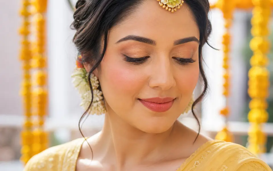 Close-up of an Indian bride in a butter-yellow outfit with sheer gold eyeshadow, soft brown liner and peachy nude lips.