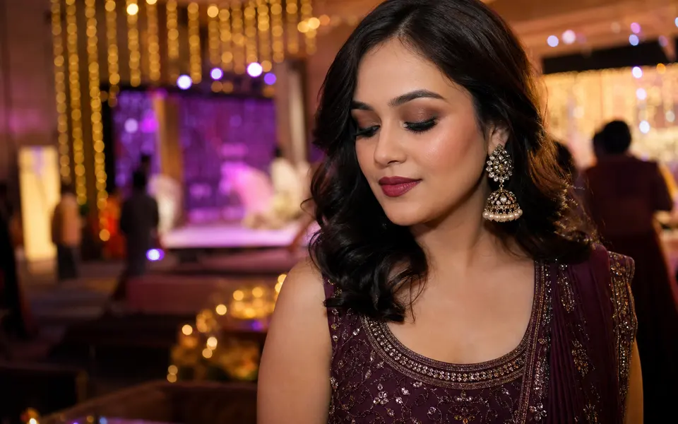 Indian wedding guest at an evening sangeet wearing a jewel-toned lehenga with classic brown smokey eyes and a balanced berry lip.